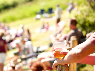 A Hand Holding A Glass Of Beer In Front Of A Crowd